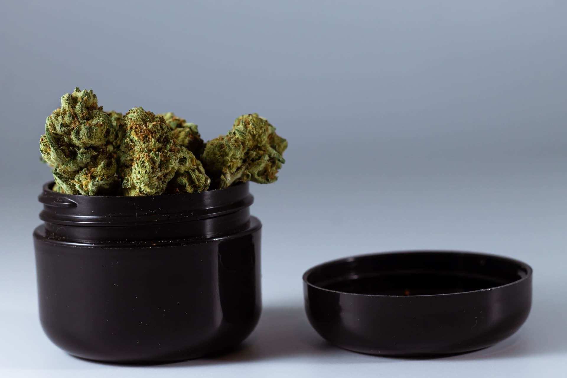 Cannabis flower in an open black protective jar with its lid beside it