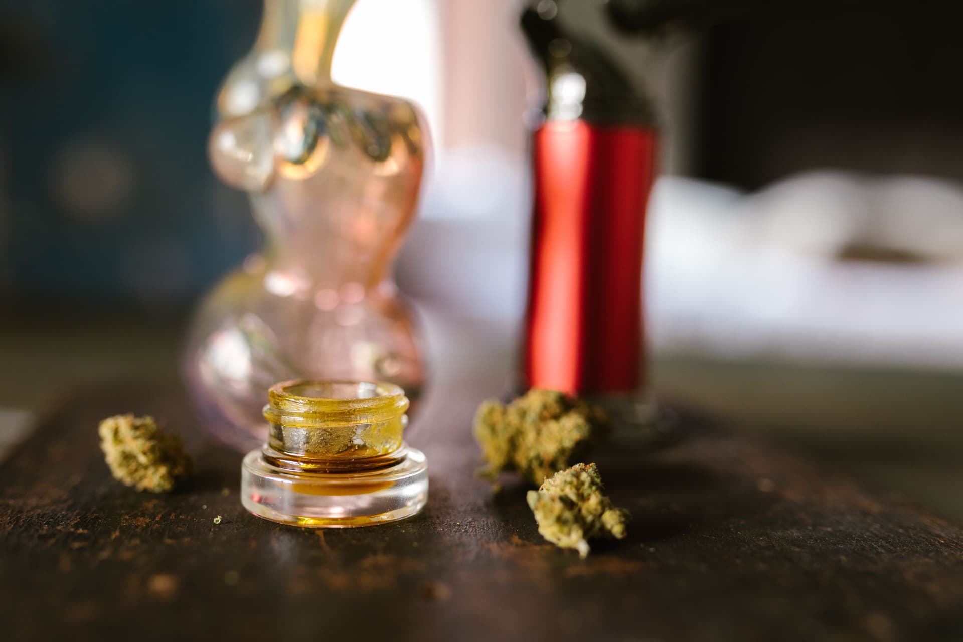 Glass jar of cannabis concentrate beside flower and handling tools